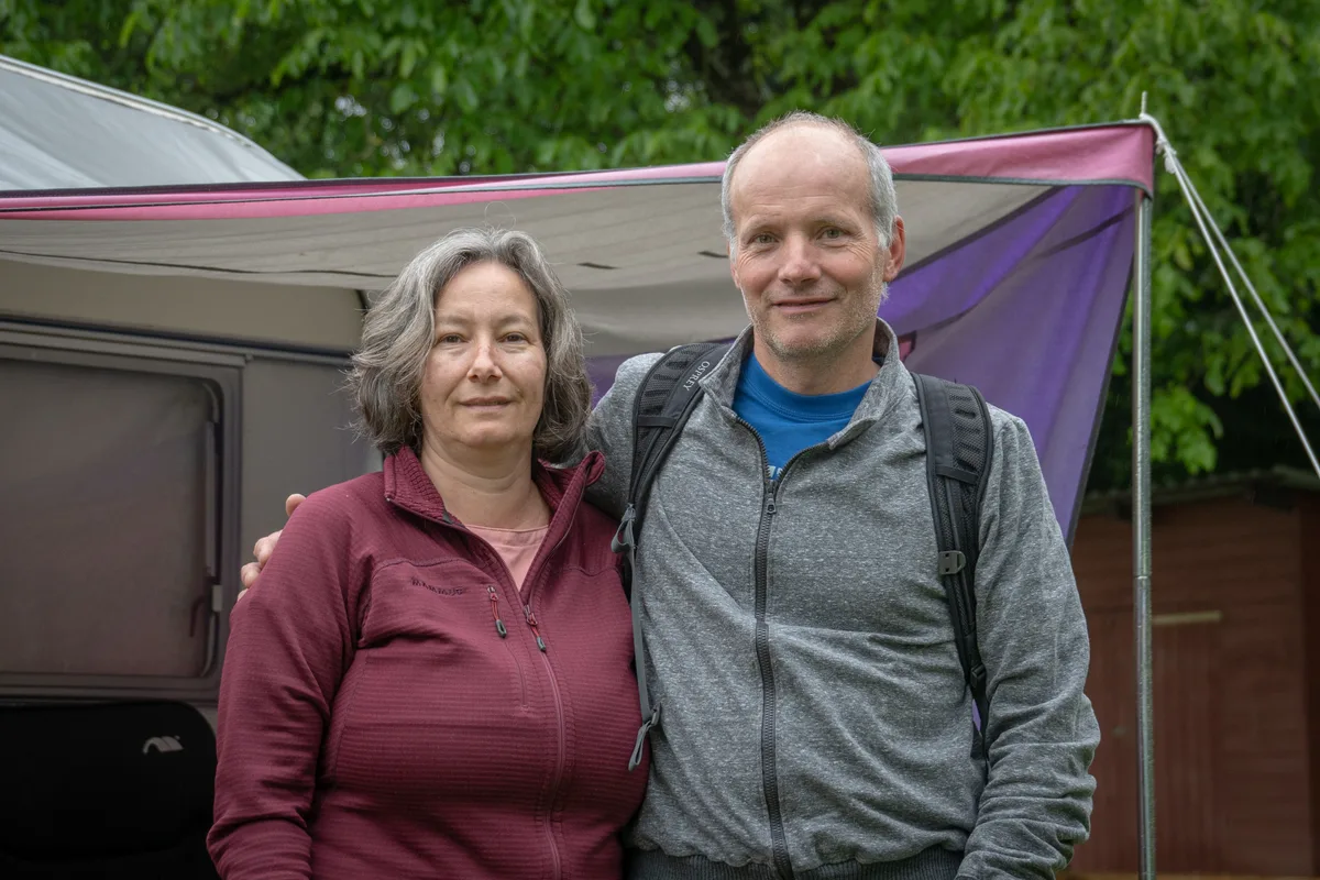 Ein Ehepaar lächelt auf einem Campingplatz in die Kamera.